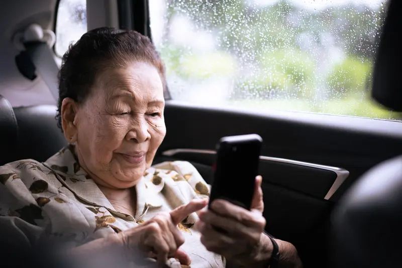 An old lady setting in the backseat of a luxuy black car using her smartphone, symbolizing Houston Elders Transportation Services.